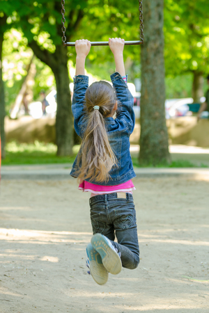 A girl is riding a metal ladder on chains in a playgroundの写真素材