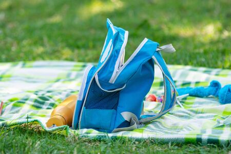 Children's backpack and bottle for water lie on a bedspread on a picnicの写真素材