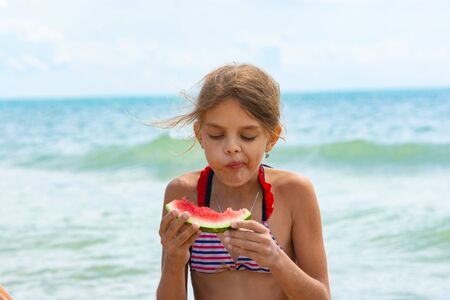 A girl eats a watermelon on the beachの写真素材