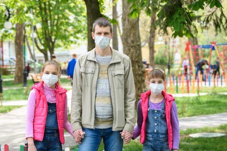 Dad and two daughters are in protective medical masks at the playgroundの写真素材