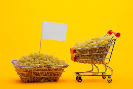 The cart and the basket are filled with pasta on a bright orange background, a flag is stuck in the basketの写真素材
