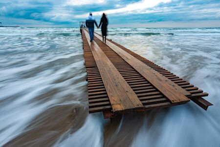 Two people go down the wooden sea pier into the distance, evening, long exposureの写真素材