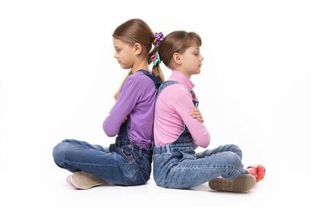 Two quarrelled girls sit with their backs to each other on a white backgroundの写真素材