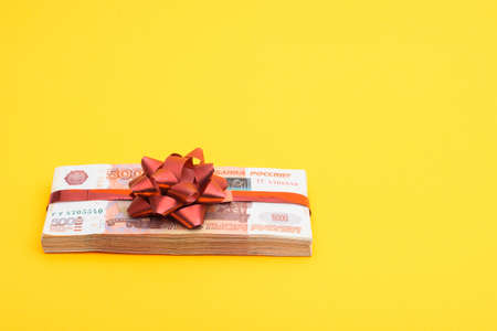 Gift pack tied with a red bow of five thousandth Russian bills on a yellow backgroundの写真素材