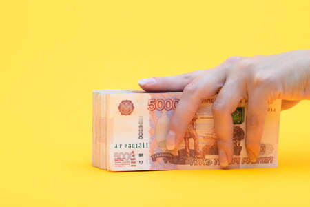 Hand covered a pack of five thousandth bills, yellow background