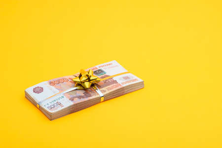 On a yellow background lies a bundle of notes with a yellow ribbon and a bowの写真素材