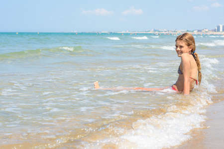 Girl swims in the waves on the sandy seashoreの写真素材