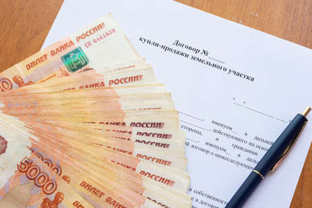 On the contract of sale of the land plot there is a bundle of money spread out in a fan and a penの写真素材