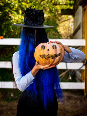A girl with her hair covered face in a witch costume is holding a pumpkin with a painted face and a witch's capの写真素材