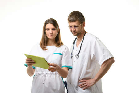 Doctor and nurse discussing the patient's tests, looking thoughtfully into the screen of a tablet computerの写真素材