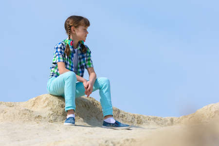 A teenage girl crouched on the top of a mountain and resting examines the surroundingsの写真素材