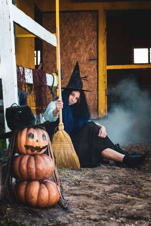 A girl dressed as a witch with a broom squatted by the fence at the Halloween celebrationの写真素材