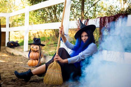 A girl dressed as a witch sits by the fence, thick white smoke creeps out from behind the fence