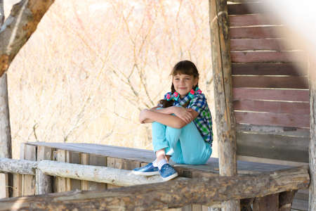 A ten-year-old girl sits in a wooden gazebo and looks cheerfully into the frameの写真素材