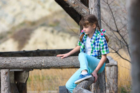 A girl tries to sit on a fence made of a thick wooden frameの写真素材