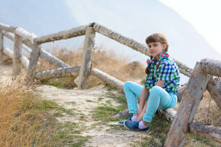 A girl sits on a fence made of a wooden blockhouse against the background of a landscapeの写真素材