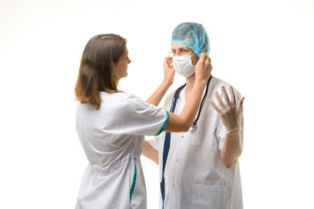 Nurse putting medical mask on surgeon face isolated on whiteの写真素材