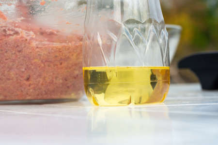 On the table is sunflower oil in a plastic bottle, in the background is a glass bowl with minced meat for cutletsの写真素材