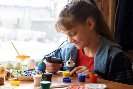 A girl glues elements to crafts with a glue gunの写真素材