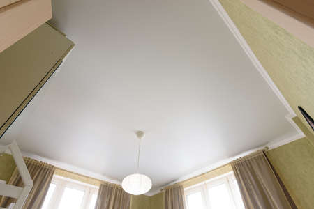 Stretch white matte ceiling close-up with a chandelier in the interior of a living bedroom