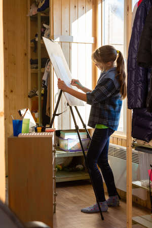 A ten-year-old girl draws with paints on an easel at homeの写真素材