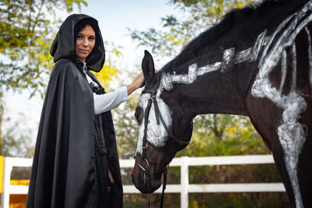 Portrait of a beautiful girl dressed in medieval style, a horse with a painted skeleton is standing next toの写真素材