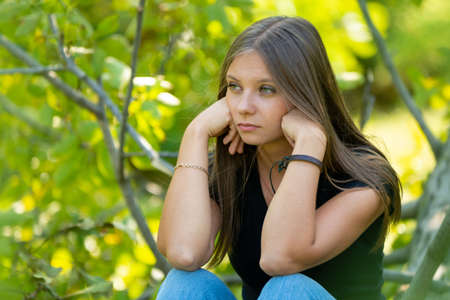 Sad girl sits on the background of foliage and sadly looks into the distanceの写真素材