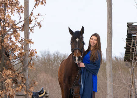 A girl in a blue dress and a horse on the background of a winter forestの写真素材