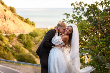 Happy newlyweds kiss against the backdrop of a beautiful mountain landscape, the girl fervently turns away from the guyの写真素材