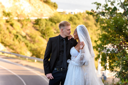 Happy newlyweds kiss against the backdrop of a beautiful mountain landscape, the girl and the guy look at each otherの写真素材