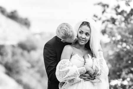 Happy newlyweds hugging against the backdrop of a beautiful mountain landscape, a guy kissing a girl, black and white versionの写真素材
