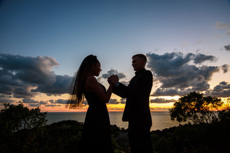 Happy young couple holding each other's hands in backlight against sunset backgroundの写真素材