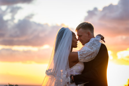 Happy newlyweds hugging against the sky in the rays of the setting sunの写真素材