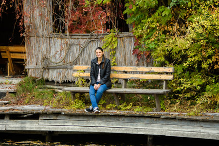 A young beautiful girl in casual clothes sits on a bench in an autumn parkの写真素材