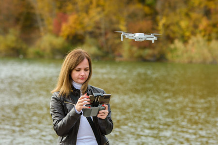 A young girl launches a radio-controlled quadcopter on the shore of an autumn lake, the girl adjusts...