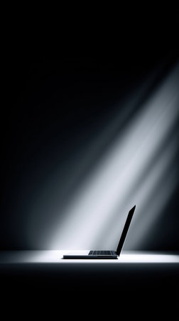 laptop illuminated by dramatic spotlight, empty desk in dark studio, soft rim light highlights keyboardの素材