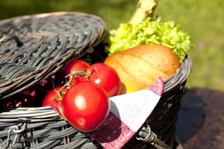 Open Picnic Basket With Tomatoes, Bread, Salad And Champagne On Old Wooden Tableの写真素材