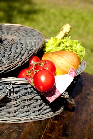 Open Picnic Basket With Tomatoes, Bread, Salad And Champagne On Old Wooden Tableの写真素材