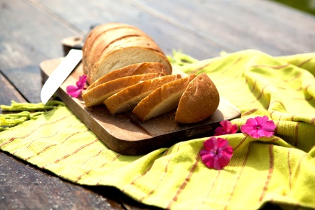 Fresh Bread On Chopping Board With Knife And Flowers On An Old Wooden Tableの写真素材