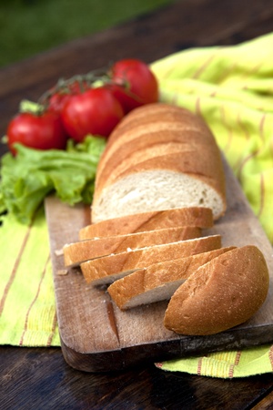 Fresh Bread On Chopping Board With Tomatoes And Salad In The Backgroundの写真素材