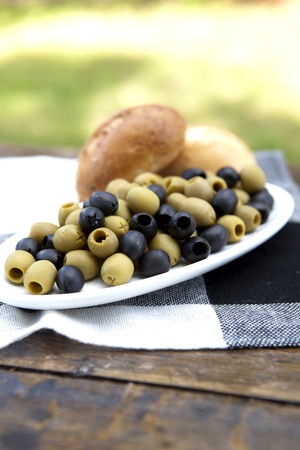 Olives On A Plate On A Old Wooden Table With Green Grass In The Backgroundの写真素材