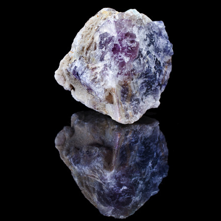 Rough unpolished specimen of fluorite crystal with reflection on black surface backgroundの写真素材