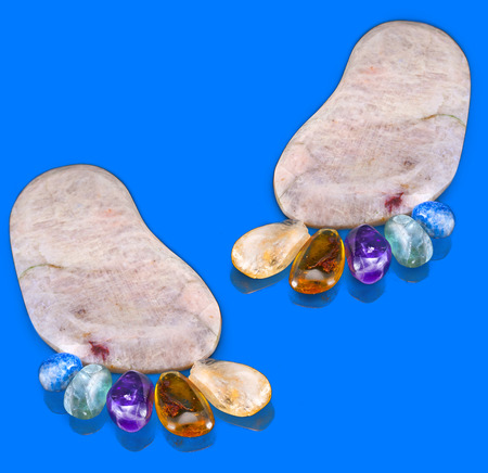 pair trace feet made of natural colorful raw gem-stones on blue surface backgroundの写真素材