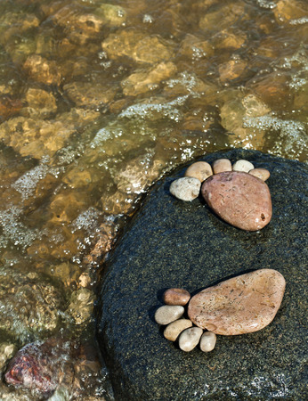 two trace feet made of a pebble stone on the sea wave top view backdropの写真素材