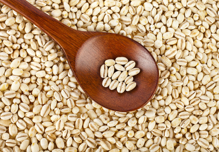 pearl barley grains in a wooden spoon close up surface top view backgroundの写真素材