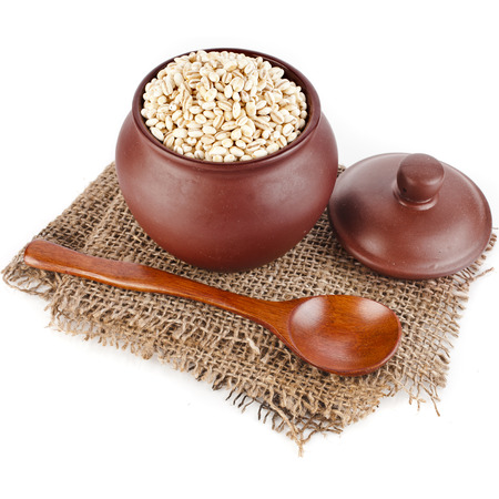 barley pearl porridge in a clay pot with a spoon isolated on white backgroundの写真素材