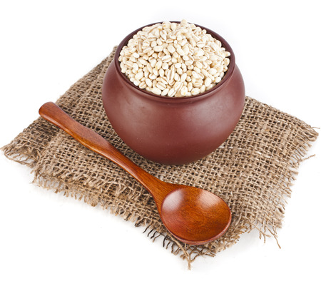 pearl barley porridge in a clay pot with a spoon isolated on white backgroundの写真素材