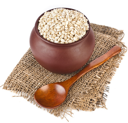 pearl barley porridge in a clay pot with a spoon isolated on white backgroundの写真素材