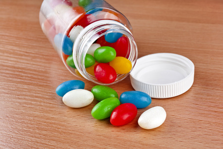Colored Pills JellyBeans pouring out of the plastic bottle on surface wooden tableの写真素材