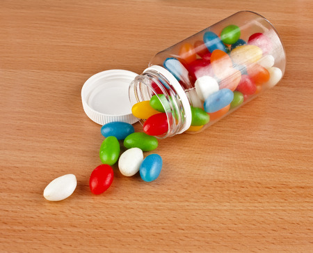 Colored Pills pouring out of the plastic bottle on surface wooden tableの写真素材
